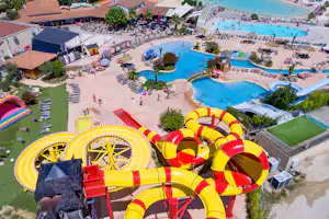 Wasserrutschen und mehrere Pools auf einem Campingplatz, mit Liegestühlen, Gebäuden und Wegen im Hintergrund.