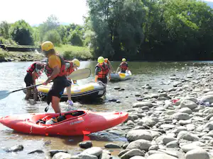 Rafting-Boote auf einem Fluss mit Kieselsteinen am Ufer, mehrere Personen mit Schwimmwesten im Schlauchboot.