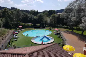 Camping-Pool im Garten mit Liegestühlen, Sonnenschirmen und eingezäuntem Becken, umgeben von Bäumen und Hügeln.