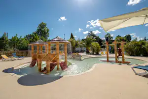 Poolbereich mit Sonnenschirm, Liegen und Holzsteg am Campingplatz, im Hintergrund Bäume und Gebäude.