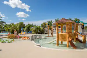 Bambus-Wasserspiel im Pool mit Planschbecken, Sonnenschirmen und Liegestühlen am Campingplatz, umgeben von Palmen.
