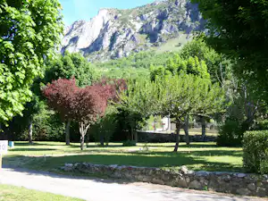 Grüne Campinganlage mit Rasen, Bäumen und Hecken; im Hintergrund ragen hohe Berge über dem Tal.