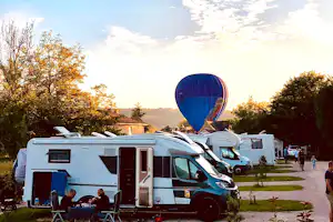 Wohnmobile auf einem Campingplatz bei Sonnenuntergang, im Vordergrund ein Camper mit Markise und Sitzgruppe.