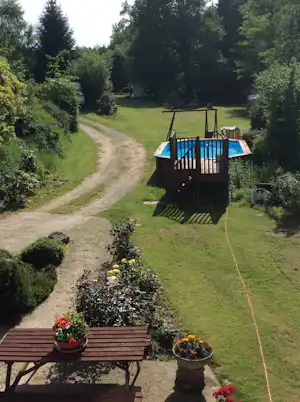 Privater Campinggarten mit kleinem Pool, Holzumrandung, Kiesweg und Bäumen, im Hintergrund Stellplätze mit Wohnwagen.