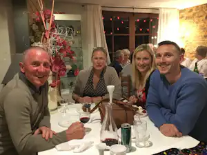 Gruppe am gedeckten Tisch im Camping-Restaurant, Gläser und Flasche auf dem Tisch, Lichterkette im Hintergrund.