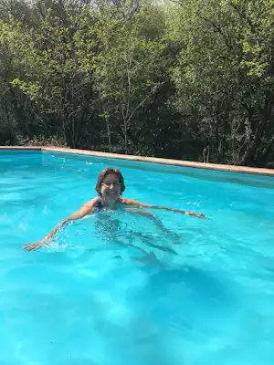 Frau im türkisfarbenen Pool, umgeben von Bäumen im Hintergrund, mit Poolrand aus Holz.