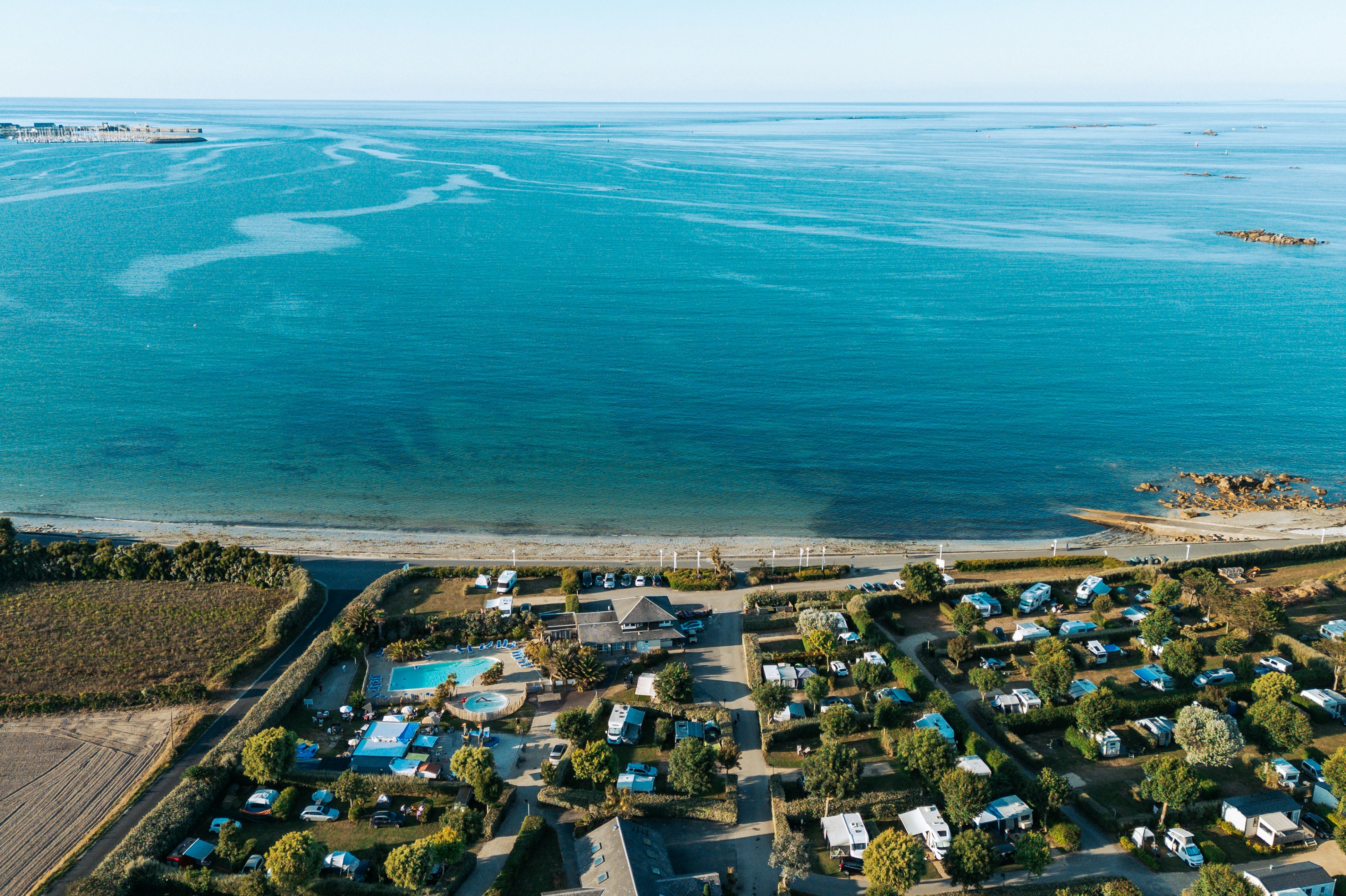 Luftaufnahme eines Campingplatzes an der Küste mit Stellplätzen, Wohnmobilen und Blick auf das Meer und den Strand.