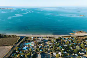 Luftaufnahme eines Campingplatzes an der Küste mit Stellplätzen, Wohnmobilen und Blick auf das Meer und den Strand.