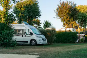 Wohnmobil auf einem Campingplatz, umgeben von Hecken und Bäumen, mit Markise und weiteren Fahrzeugen im Hintergrund.