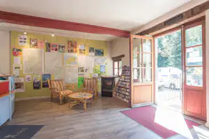 Rezeption im Campinghaus mit Sitzgelegenheiten, Infowand und Karten an den Wänden, offene Tür zum Außenbereich.
