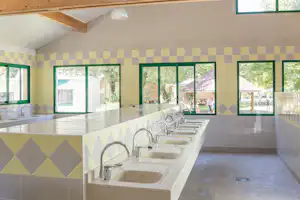 Waschraum im Campingbereich mit mehreren Waschbecken, Fliesenwand und großen Fenstern zur Terrasse.
