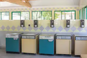 Mehrere Geschirrspüler in einer Camping-Gemeinschaftskueche mit Fliesenwaenden, Gruen-Weiss-Rauten und Fenstern.