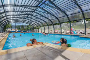 Überdachtes Schwimmbecken im Campingbereich mit Glasbogen-Dach, Liegen und mehreren Personen im Wasser.
