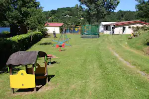 Grüne Wiese auf dem Campingplatz mit Spielgeräten, Gartenwegen und mehreren Wohnwagen bzw. Mobilheimen im Hintergrund.