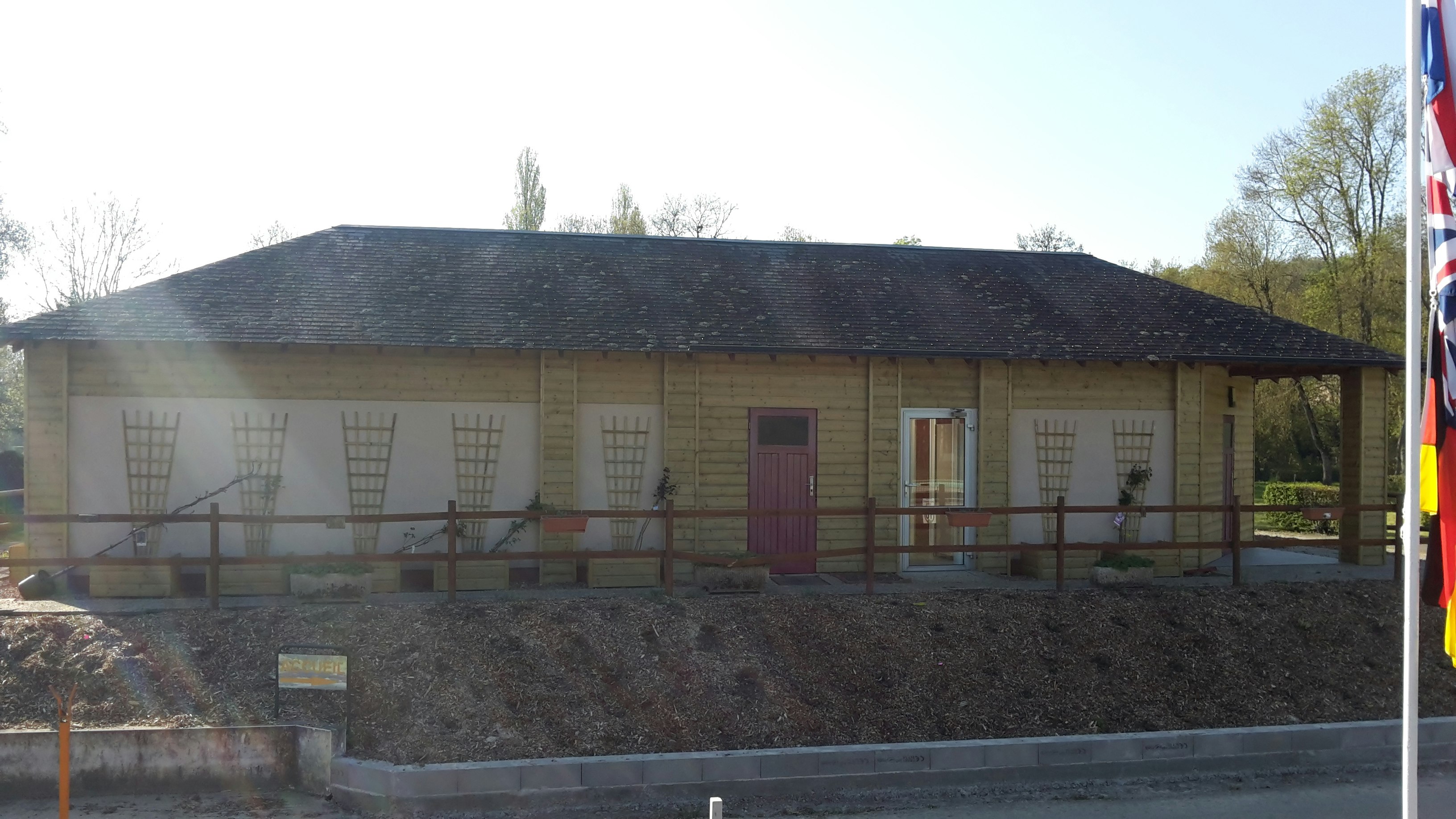 Holz-Campinghaus mit Terrasse, Fenster und Eingangstür, davor ein Weg und ein kleiner Gartenbereich.
