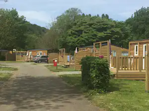 Holzbungalows auf einem Campingplatz, mit Holzterrassen, Hecken und einem Weg zwischen den Unterkünften.