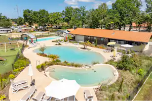 Schwimmbecken mit Liegen und Sonnenschirmen, daneben Bungalows mit Ziegeldach und Bäumen im Hintergrund.
