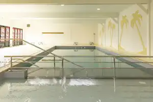 Innenpool mit Glasgeländer, Treppe und Palmenwand an der Seite, im hellen Gebäude.