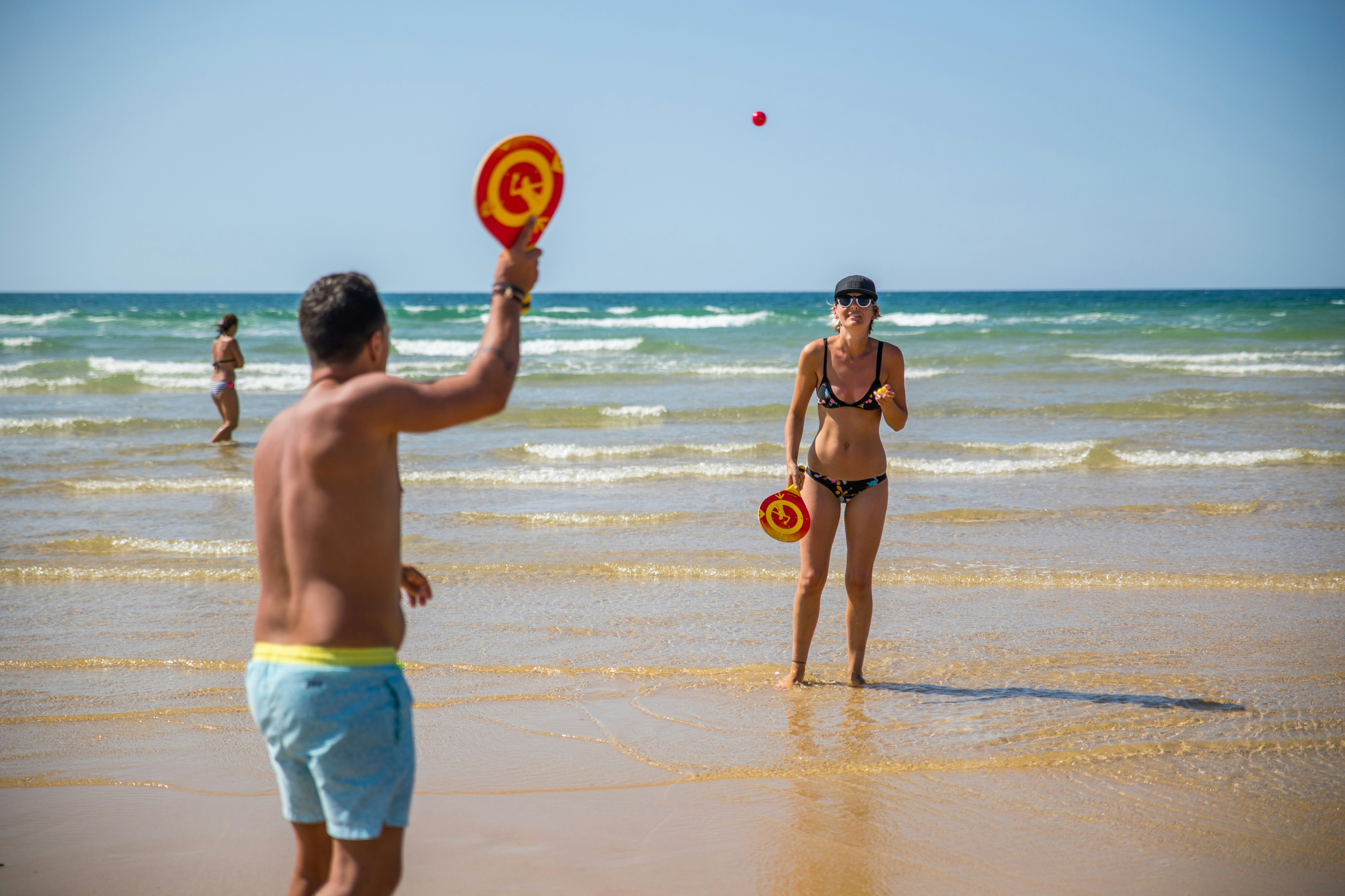 Mann und Frau am Strand mit Schwimmringen im Wasser, Blick auf die Wellen und den Sandstrand am Meer.