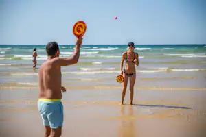 Mann und Frau am Strand mit Schwimmringen im Wasser, Blick auf die Wellen und den Sandstrand am Meer.