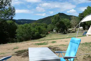 Zelt auf einem Campingplatz-Stellplatz mit blauem Stuhl und Tisch, Rasenfläche, Bäumen und Hügeln im Hintergrund.