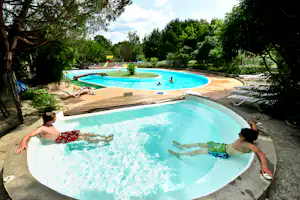 Camping Le Village du Port - Poolbereich vom Campingplatz im Grünen mit Whirlpool und Liegestühlen, Spielplatz im Hintergrund