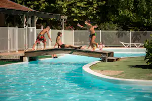 Familie am Campingpool: Kinder und Erwachsene planschen im Wasser, Holzsteg und Zaun im Hintergrund.