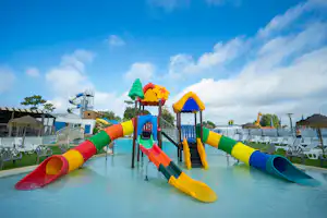 Bunter Wasser-Spielplatz mit mehreren Wasserrutschen im Campingbereich, daneben Liegestühle und ein Gebäude am Rand des Pools.