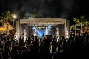 Menschenmenge vor einer beleuchteten Bühne mit Lichterketten und Stern-Dekoration auf einem Campingplatz bei Nacht.