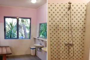 Camping-Badezimmer mit Dusche, Duschkopf und Fliesenwand sowie Waschbecken und Fensterblick ins Grüne.