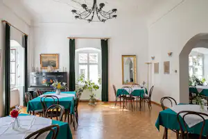 Esszimmer im Campingbereich mit gedeckten Tischen, Stühlen, grünen Vorhängen und Kronleuchter an der Decke.