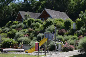 Camping Les 12 Cols - Kinderspielplatz auf mit Rutsche und Kletternetz mit Hütten auf einem Hügel im Hintergrund