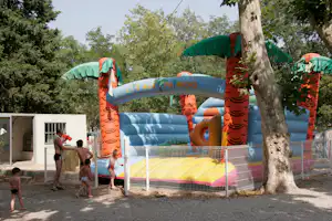 Aufblasbares Kinder-Springhaus mit bunten Säulen und Rutsche, im Freien am Campingplatz, umgeben von Bäumen.