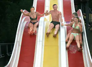 Menschen auf einer bunten Wasserrutsche im Campingbereich, mit weißem Rand und rotem sowie gelbem Rutschenteil.