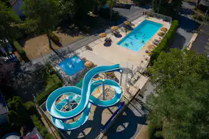 Blaue Camping-Pools mit Rutschen und zwei Becken auf einer Sonnenterrasse, umgeben von Bäumen und Wegen.