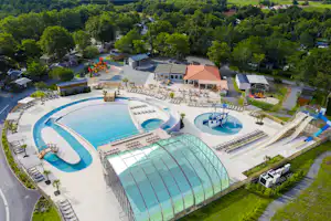 Luftaufnahme eines Campingplatzes mit großen Schwimmbecken, Sonnendecks, Liegen und einem beheizten Innenpool.