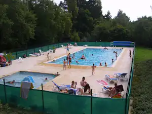 Großer Camping-Pool mit vielen Badegästen, Liegen und Sonnenschirmen, umgeben von Bäumen und einem grünen Zaun.