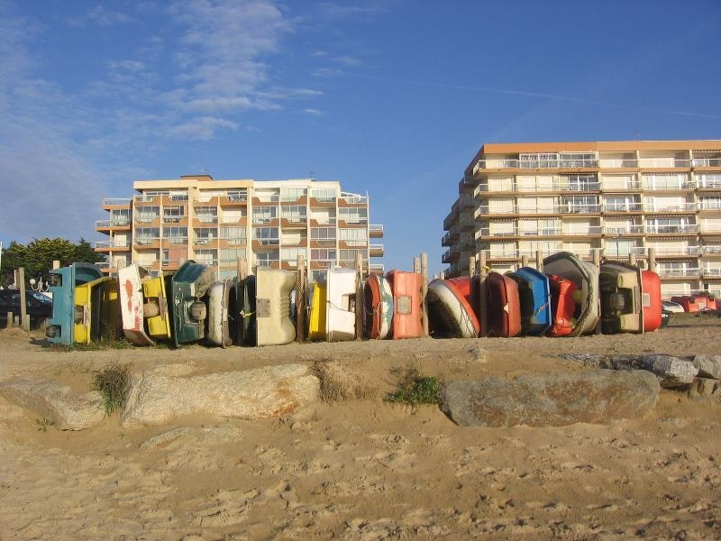 Reihe von Strandduschen und Bungalows am Campingplatz, dahinter mehrstöckige Gebäude und ein Sandweg.