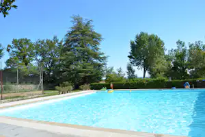 Blauer Camping-Pool mit Schwimmspielzeug am Beckenrand, umgeben von Bäumen und Hecken im Garten.