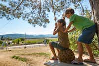 Camping Les Bastets - Kinder die auf einer Seilrutsche spielen mit Kleinfeldfussballplatz im Hintergrund