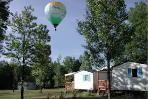 Bunte Heißluftballon am Himmel über einem Campingplatz mit Wohnwagen und Mobilheimen zwischen Bäumen und Rasen.