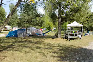 Campingplatz im Grünen: Zelte zwischen Bäumen, daneben ein Grilltisch und ein Pavillon mit Sitzgelegenheiten.