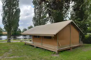 Zelt auf Holzpodest am Campingplatz, mit Vorzelt und Blick auf den Fluss zwischen Bäumen.