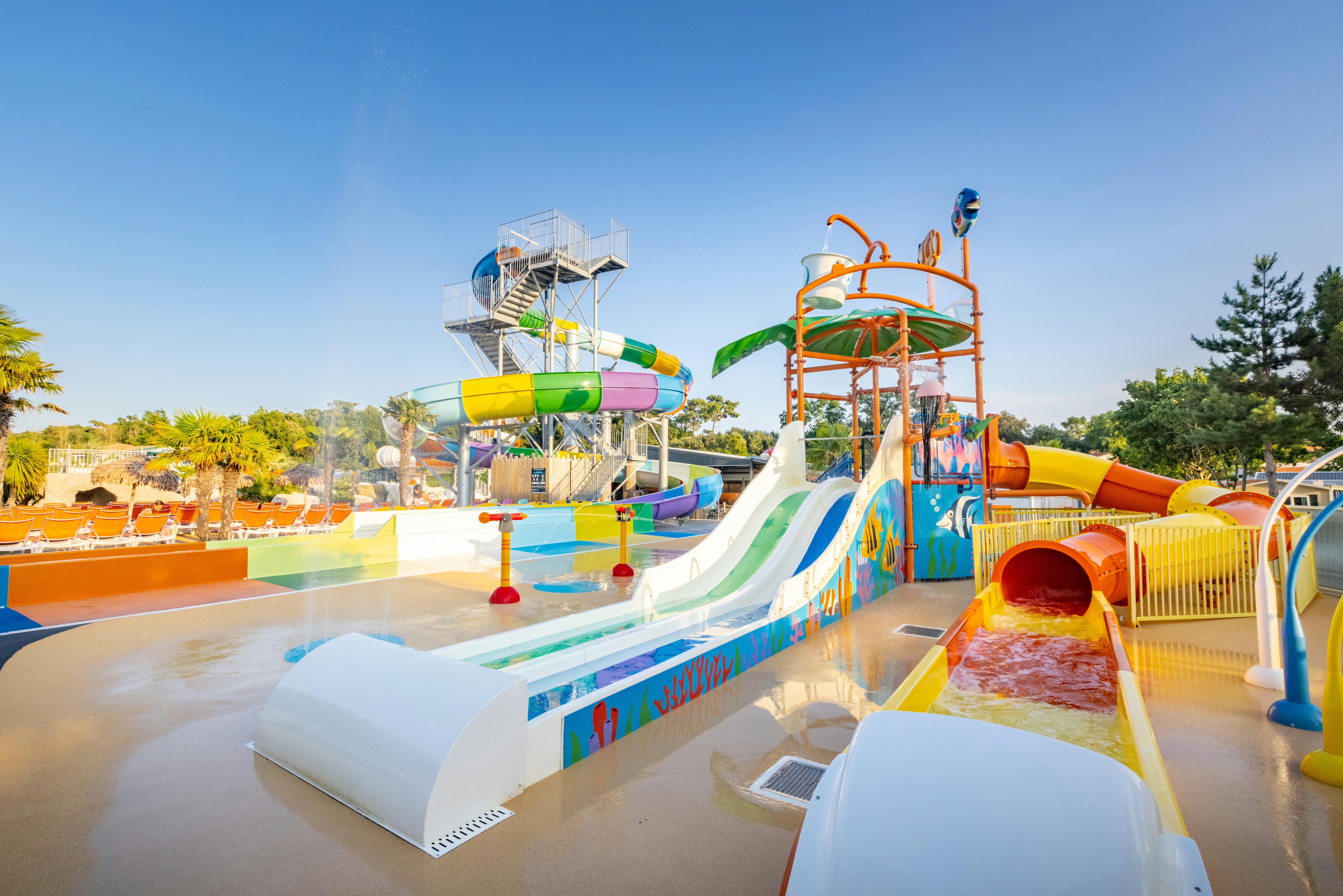 Wasserrutschen und Planschbecken auf einem Campingplatz, mit bunten Rutschen, Geländern und Wasser im Becken.