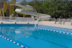 Schwimmbecken mit blauen Bahnen und Sprungbrett, daneben ein Rutschenbereich mit großen Wasserrutschen und Geländer.