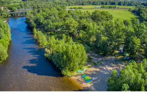 Fluss mit grünem Ufer und Wald, daneben ein Campingbereich mit mehreren bunten Liegen am Ufer.
