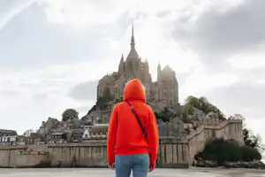 Person im roten Hoodie steht vor einer großen Kathedrale auf einem Hügel, umgeben von Häusern und einer Mauer.