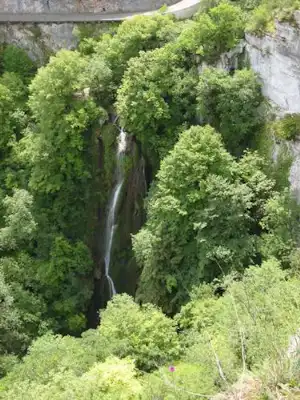 Wasserfall in einem grünen Tal, umgeben von dichtem Laub und Felsen an der steilen Wand.