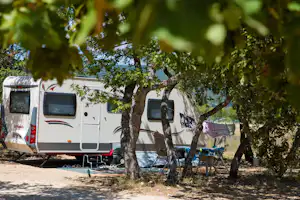 Wohnwagen auf einem Campingplatz zwischen Bäumen, mit Vorzelt und Campingstühlen am Stellplatz.