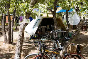 Fahrräder stehen auf einem Campingplatz zwischen Bäumen, im Hintergrund ein Zelt und ein Schild mit der Nummer 125.